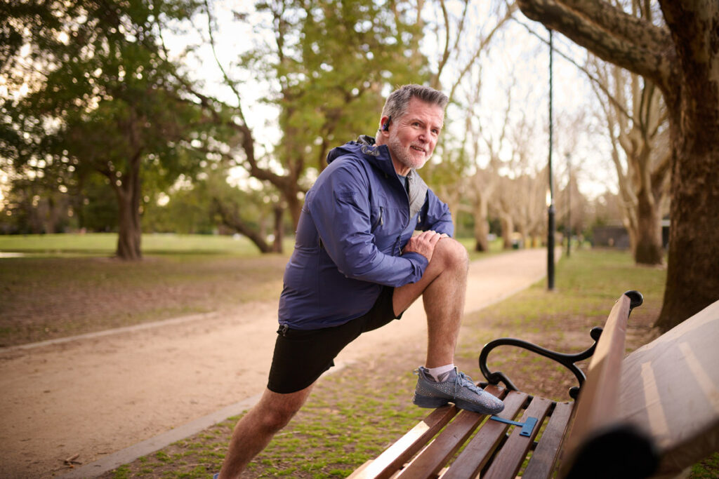 A man in running clothes stretching at a bench