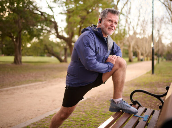 A man in running clothes stretching on a park bench.